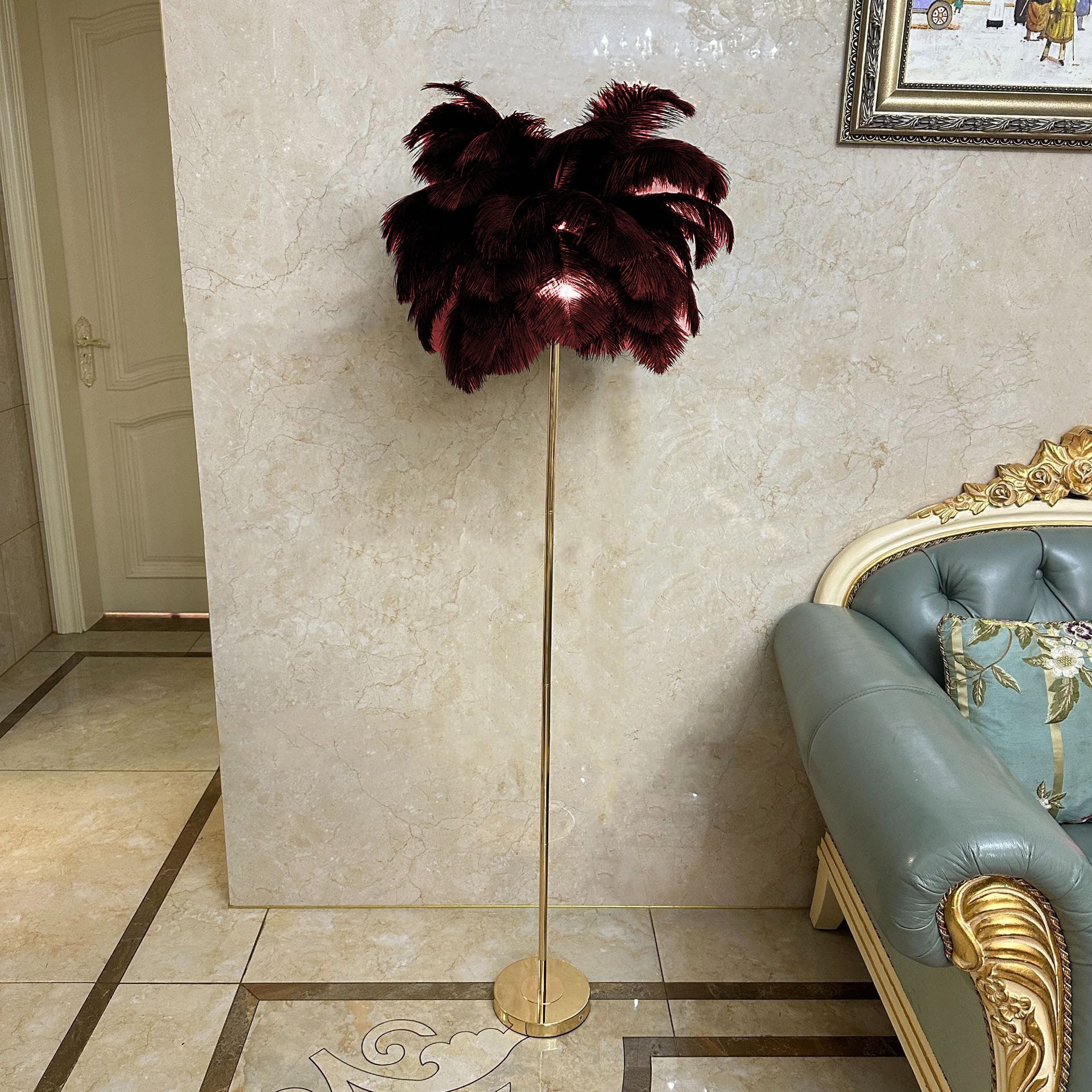 Stehlampe mit roten Straussenfedern und goldenem Ständer neben einem blauen Sofa und beiger Wand